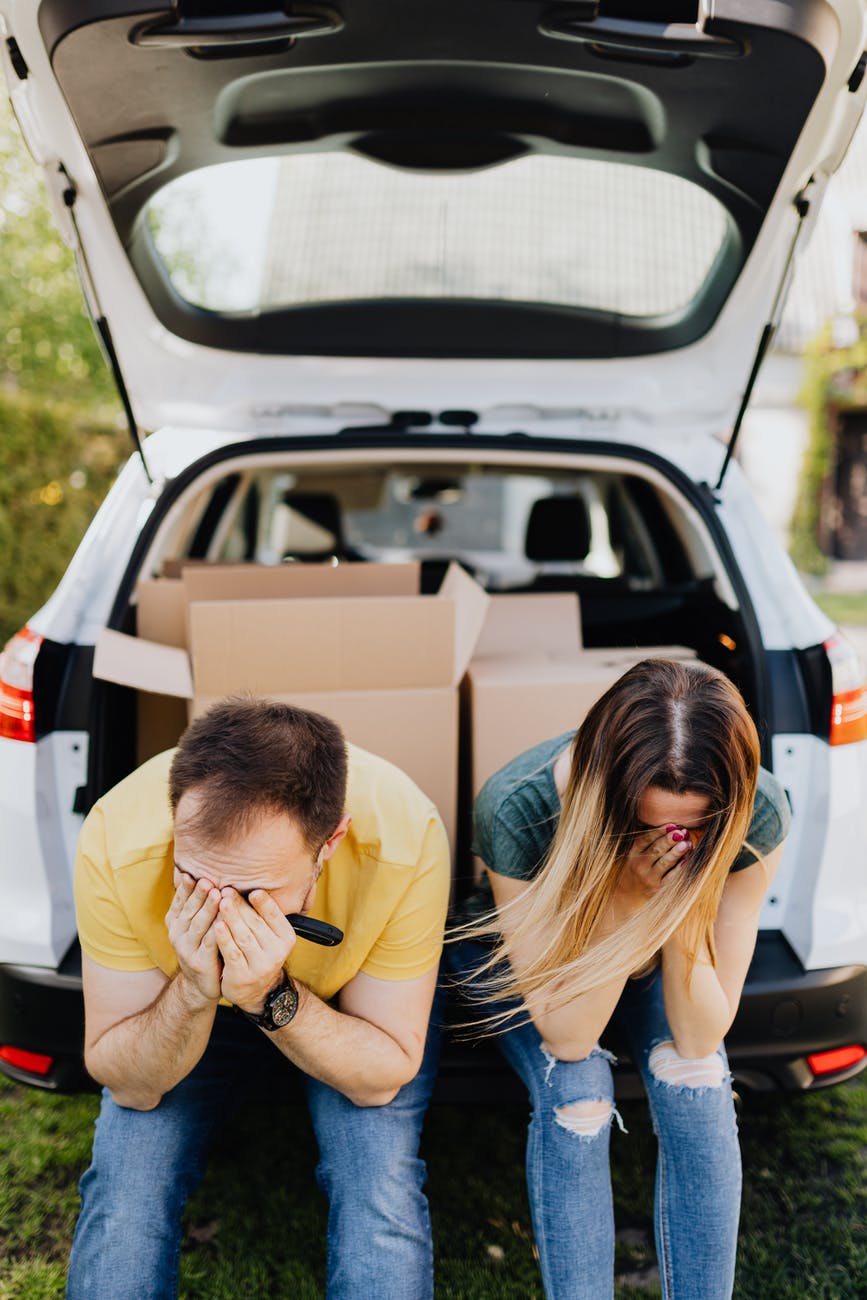 tired couple sitting on car luggage boot